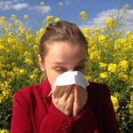 woman blowing nose with yellow flowers behind her